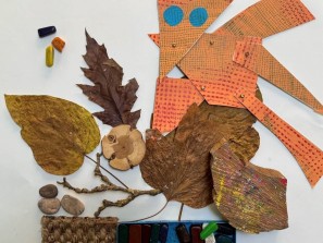 Blätter, Steine, Äste und bunt bedrucktes Papier auf weißem Untergrund.