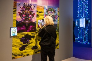 Eine Besucherin steht vor Werken in der Ausstellung und schaut auf ihr Smartphone.