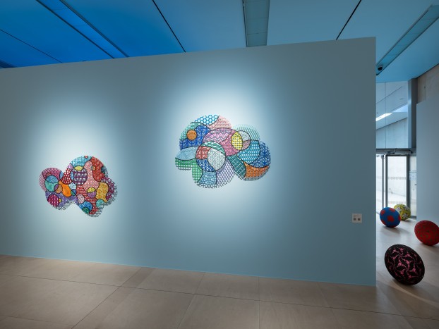 An installation view with cloud-shaped artworks in front of a blue wall