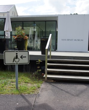 Das Bild zeigt ein Hinweisschild zum barrierefreien Eingang des Max Ernst Museums